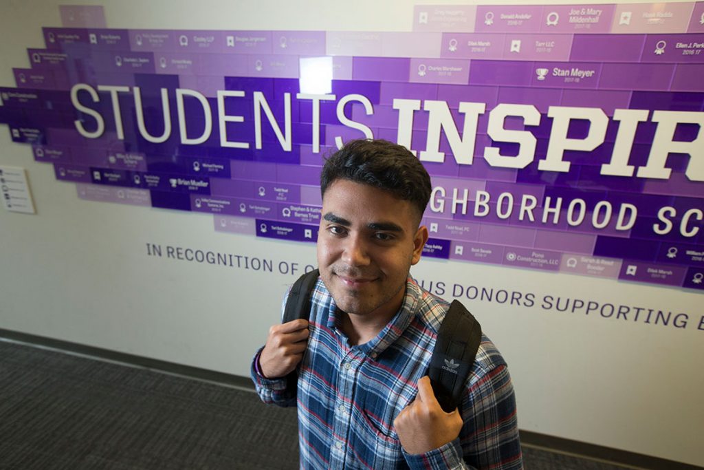 Young man named Jose Monarrez smiling in front of SIS sign.