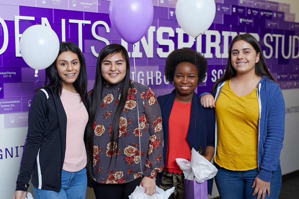 Four girls posing in front of the Students Inspiring Students wall sign