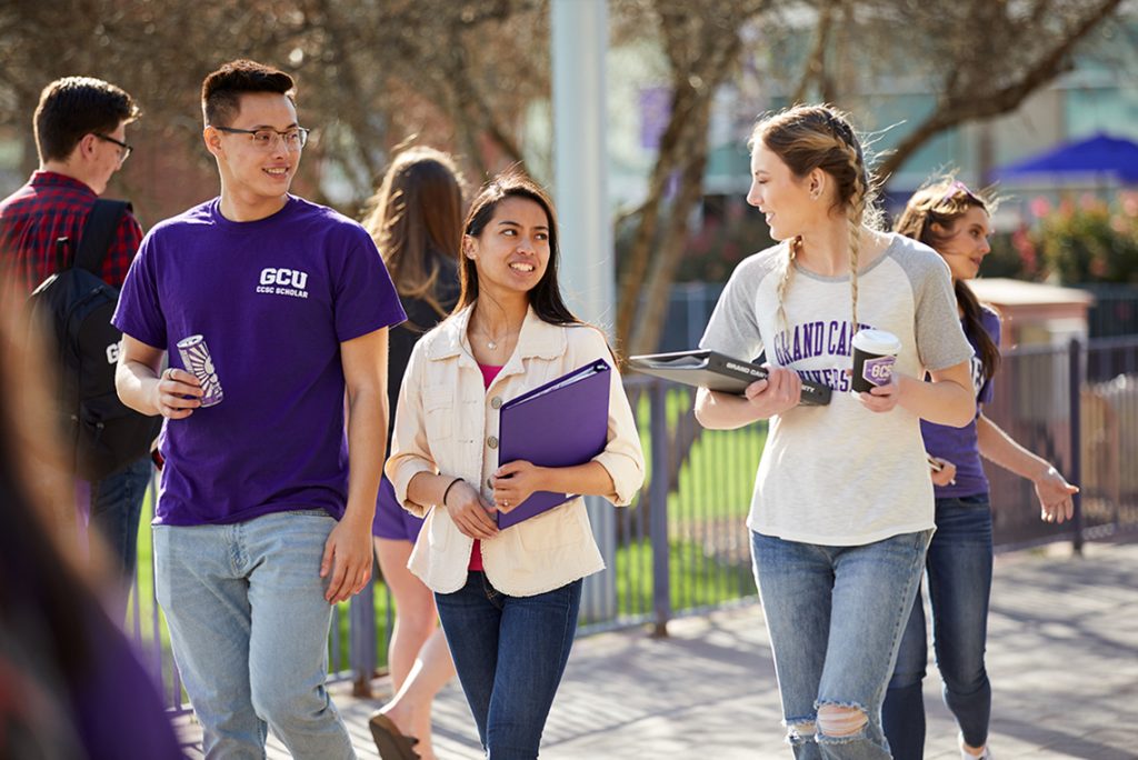 One male and two female students walking on campus promenade talking.